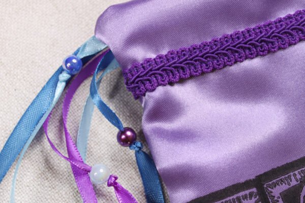 Close Up of Bastet Pouch showing purple, dark and light blue ribbons, iridescent blue and pearl purple plastic beads brocade