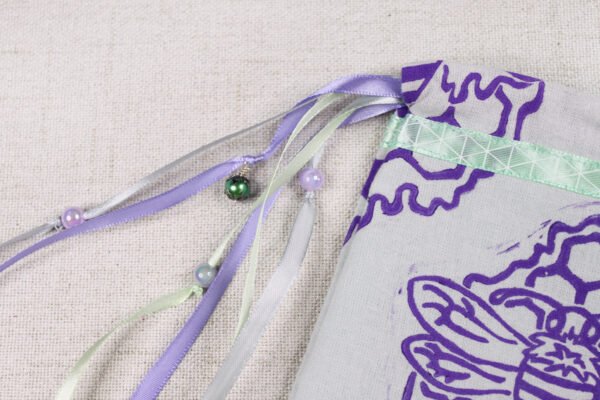Close Up of bee Pouch with mint, purple and grey ribbons, iridescent purple, silver plastic beads and green glass bead charms