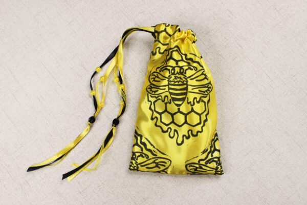 Closed yellow handprinted fabric drawstring bag with bee and honey insect print with ribbons and beads splayed out