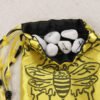 Yellow poly-satin bee pouch with black poly-satin lining, white rune stones that spell Imogen are sitting in the pouch