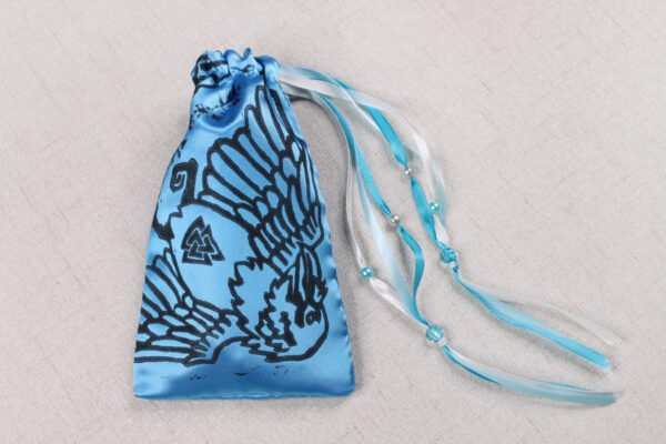 Closed turquoise handprinted fabric drawstring bag with Hugin and Munin print with ribbons and beads splayed out