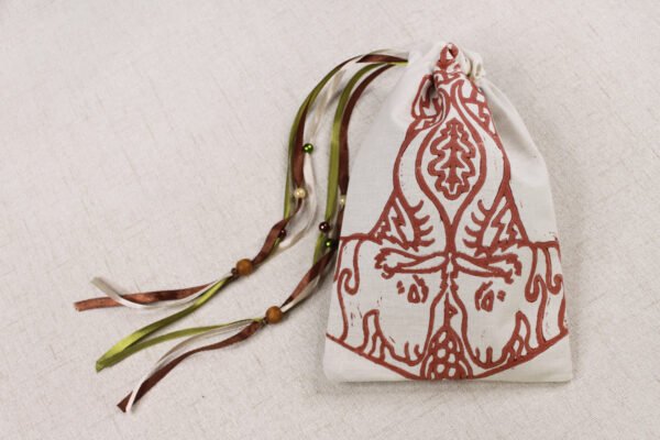 Closed cream handprinted fabric drawstring bag with Mjollnir, oak leaf and goat print with ribbons and beads splayed out
