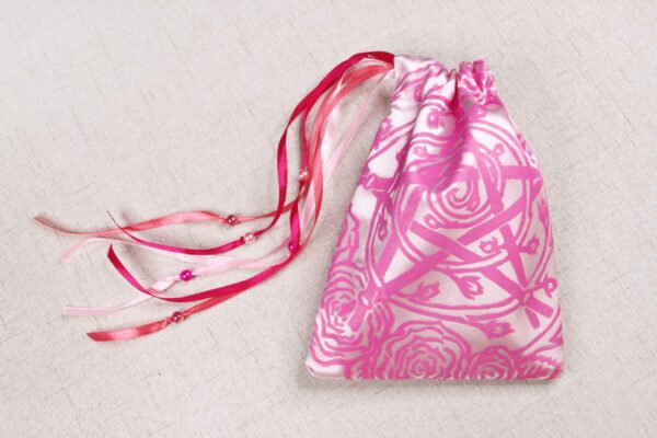 Closed pink handprinted fabric drawstring bag with Pentagram, spiral and roses print with ribbons and beads splayed out