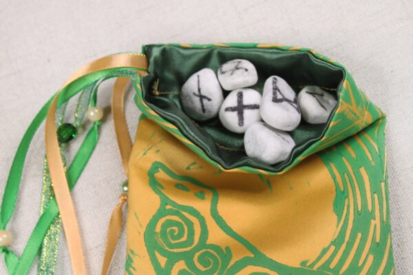 Gold poly-satin Selkie Beast pouch with dark green poly-satin lining, white rune stones spelling Imogen are sitting in pouch