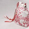 Closed standing cream handprinted fabric drawstring bag with spotted red white mushroom print with ribbons and beads to side