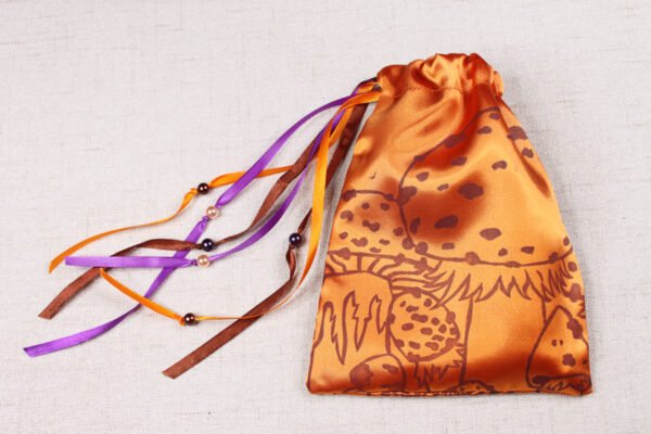Orange handprinted fabric drawstring bag with magic faerie toadstool print closed with colourful ribbons and beads spread out