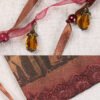 Close Up of Bastet Pouch with brown and red ribbons, amber glass metal bead charms, pearl red glass beads and brown lace band