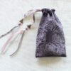 Purple handprinted fabric drawstring bag with spiralling tree print closed with colourful ribbons and beads splayed out