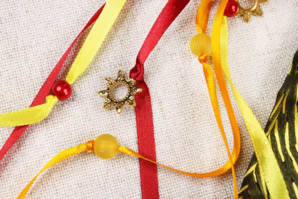 Close Up of Glastonbury Tor Pouch with red, yellow and orange ribbons, yellow and red plastic beads and gold metal sun charms