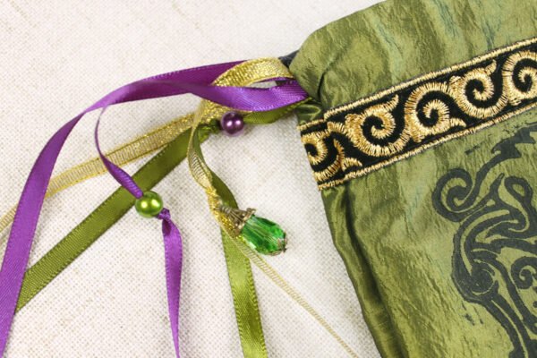 Close Up of Wild Boar Pouch with purple, gold, green ribbons, purple and green beads, green glass charms and spiral brocade