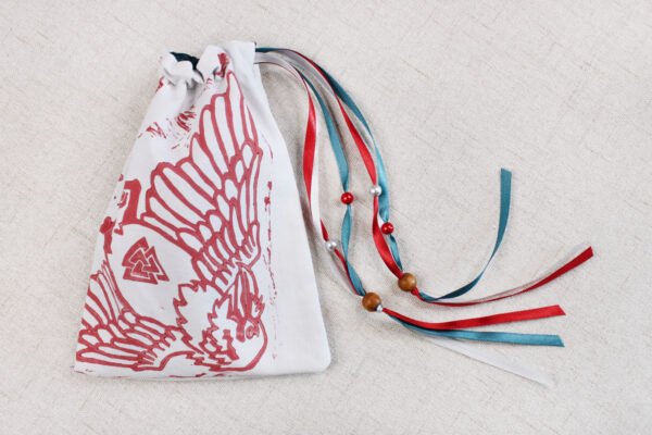 Closed white handprinted fabric drawstring bag with Hugin and Munin print with ribbons and beads splayed out