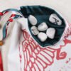 White cotton huginn, muninn, valknut pouch with teal poly-satin lining, rune stones spelling Imogen are sitting in the pouch