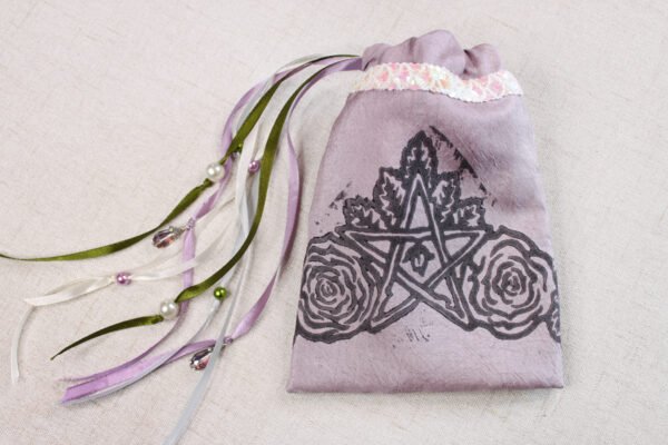 Closed purple handprinted fabric drawstring bag with Pentagram, leaves and roses print with ribbons and beads splayed out