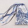 White handprinted fabric drawstring bag with blue spiralling seal print closed with colourful ribbons and beads splayed out