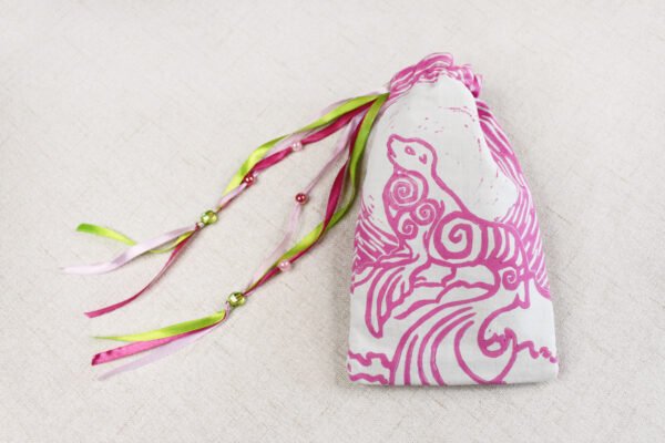 White handprinted fabric drawstring bag with spiralling seal print closed with colourful ribbons and beads splayed out