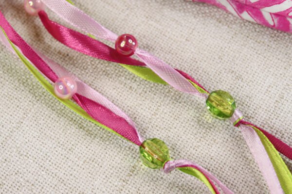 Close Up of Selkie Pouch magenta, light pink and green ribbons, iridescent pink plastic beads and clear green plastic beads