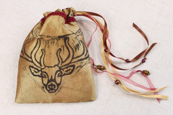 Gold handprinted fabric drawstring bag with stag antler deity print closed with colourful ribbons and beads splayed out