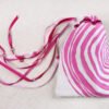 White handprinted fabric drawstring bag with ripple tree ring print closed with colourful ribbons and beads splayed out