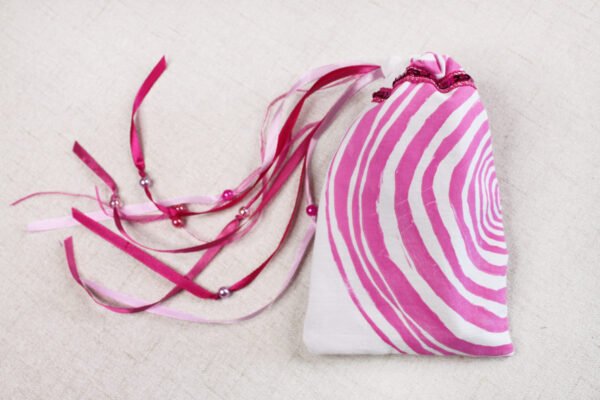 White handprinted fabric drawstring bag with ripple tree ring print closed with colourful ribbons and beads splayed out
