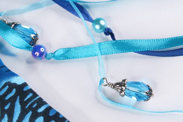 Close Up of Moon Pouch showing turquoise and dark blue ribbons, pearly blue plastic beads and metal and glass bead charms