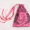 Pink handprinted fabric drawstring bag with Moon Gate and Stars print closed with colourful ribbons and beads splayed out