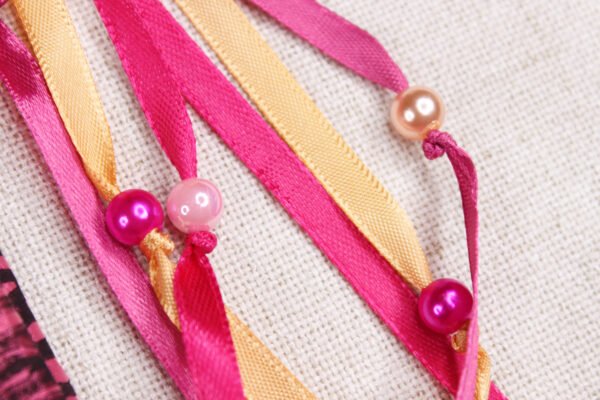 Close Up of Moon Pouch showing pink and gold coloured ribbons, iridescent pink, pearly pink and magenta plastic beads
